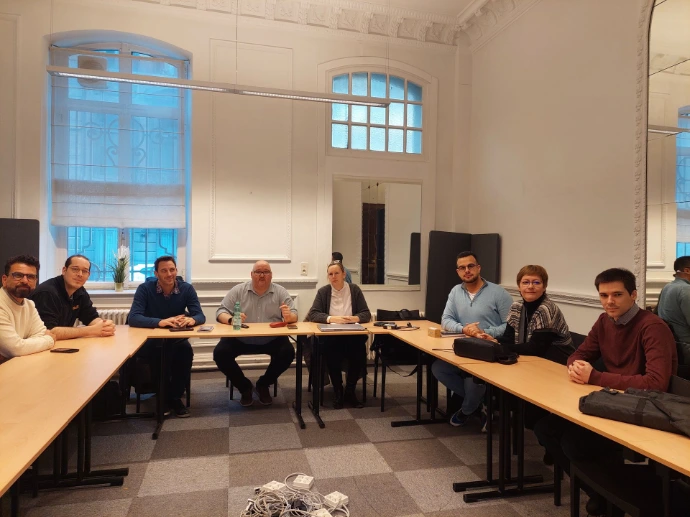 Cinq collaborateurs réunis autour d'une table en U dans une salle de réunion spacieuse aux murs moulurés et grandes fenêtres.
