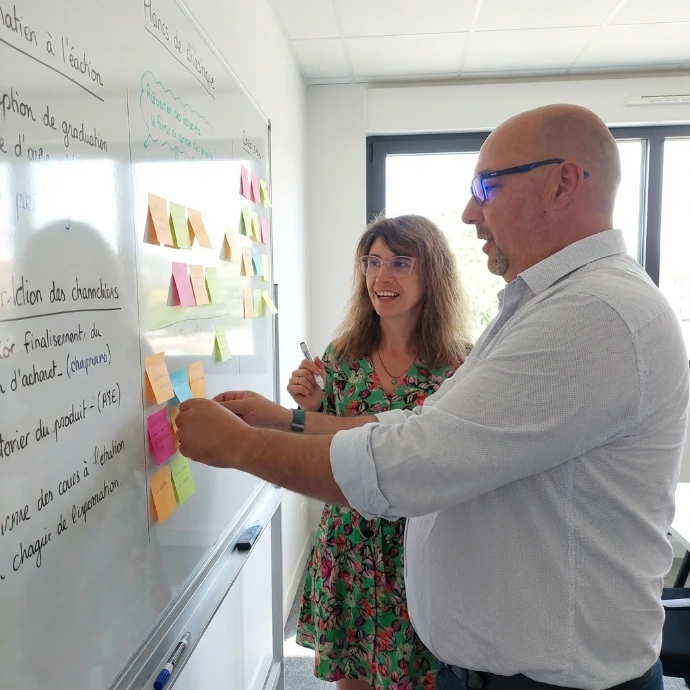 Un homme et une femme collaborent devant un tableau blanc rempli de notes et de post-its colorés lors d'une séance de brainstorming en entreprise.