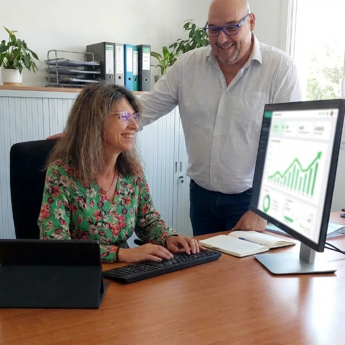 Une femme et un homme devant un écran d'ordinateur affichant des graphiques de résultats positifs dans un bureau rangé.